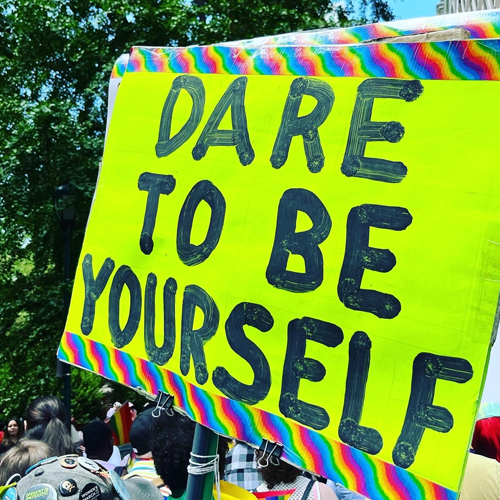 A neon green sign painted with the phrase 'Dare to be Yourself."